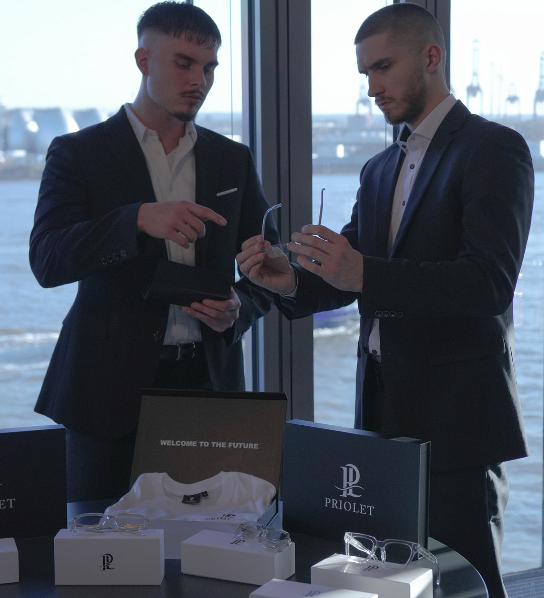 Zwei Gründer von Priolet präsentieren elegante Luxusbrillen im Showroom mit Blick auf den Hamburger Hafen.