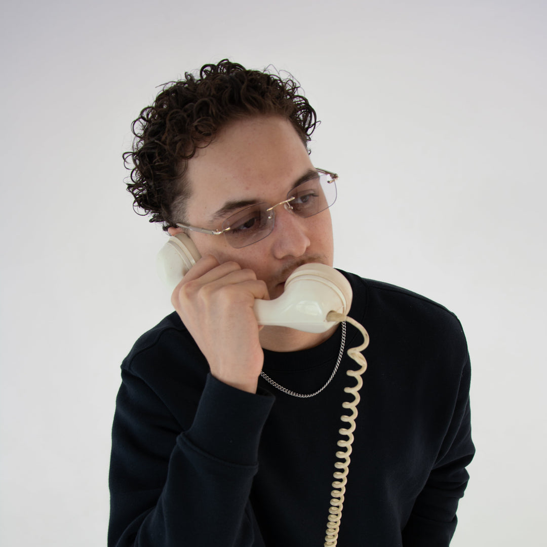 Model mit Asteria Midnight Brille in Gold – Unisex-Design mit phototropen Gläsern, stilvoller Look und Vintage-Telefon als Accessoire